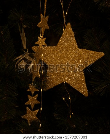 one big golden star and a garland of little golden stars hanging on a Christmas tree