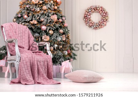 Christmas home interior in soft pink colors with gorgeous knit blanket on old style chair and decorated Christmas tree