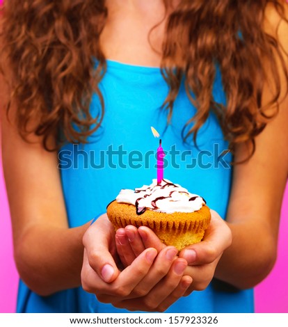 Lovely girl holding in hands cupcake with one candle, body part, happy holiday celebration, birthday party, fun and joy concept 