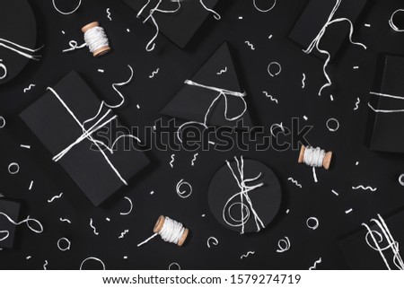 Festive presents and confetti top view. Minimalistic New Year gift boxes on black backdrop Wrapped surprises from above. Simple packages, thread and serpentine composition