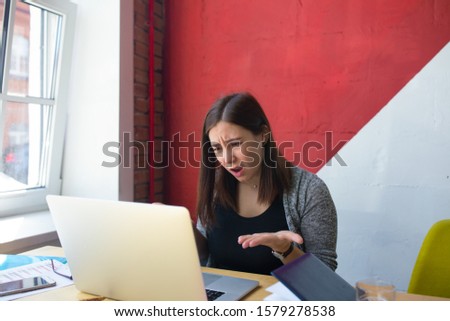 Angry business woman screaming and talking during online video conference on laptop computer while sitting in office interior 