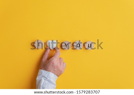 Male hand making an I love you sign spelled on wooden cut circles with marble heart shape in the middle. Over yellow background.