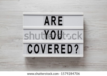 'Are you covered?' words on a modern board on a white wooden background, top view. Overhead, from above, flat lay. Close-up.