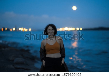 Young brunette woman at night at a place where river meets the sea in port - Visible full moon