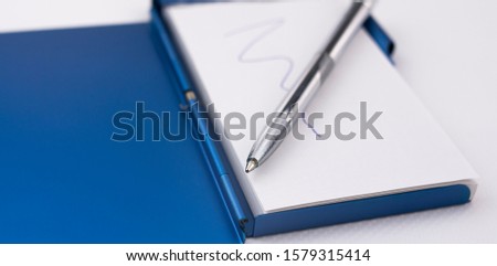 Hold a pen on a notebook to write down ideas and reminders on white paper and blue metal case