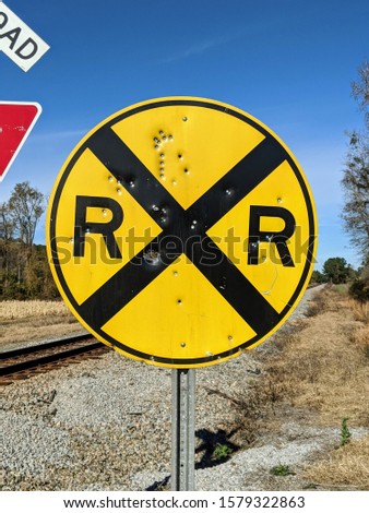 yellow railroad crossing sign with bullet holes