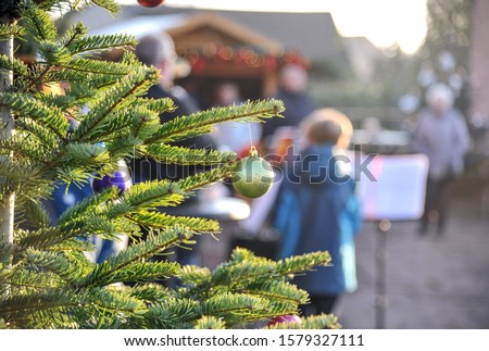 Closeup of a Christmas tree with decorations, in the background young and old musicians with music stands and market - selective focus