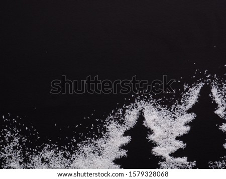 Christmas trees, wintertime. Two white Pine trees silhouette, form with snow made of rice around isolated on Black background.