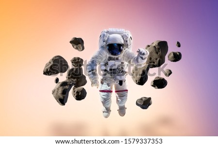 Cosmonaut with stones and asteroids on glowing background. Astronaut floating. Elements of this image furnished by NASA.