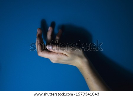 
Female hand with shadow in background, on blue background