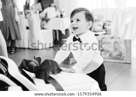 little boy in stylish clothes smiling and standing near the car on black and white photo. guests and restaurant.