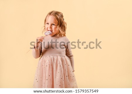 little baby with candy. Pink elegant dress. Holiday or birthday. Sweets in the hand. on a light background in the studio
