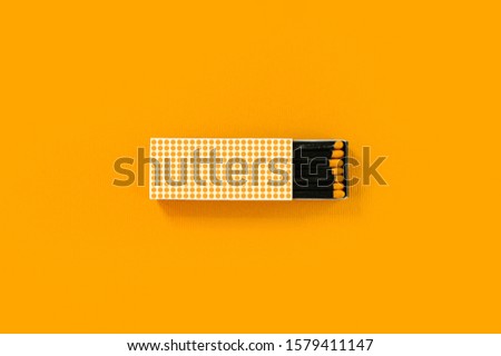 Black wood matches with yellow heads in creative dotted paper box on bold yellow background.