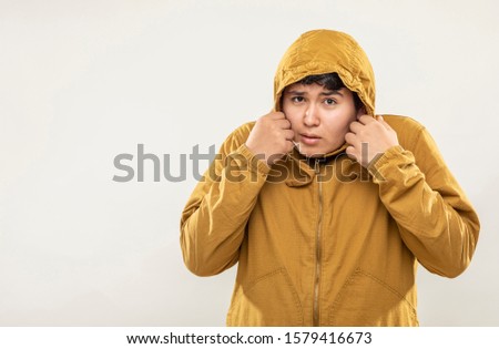 Young teenage man with yellow sweatshirt with scared face expression on gray background.