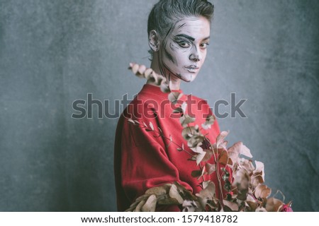 Portrait of beautiful stylish girl with creative face art (skeleton) and decorative flowers in her hands against grunge wall