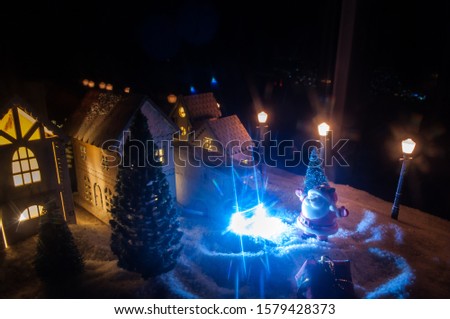 Little decorative cute small houses in snow at night in winter, Christmas and New Year miniature house in the snow at night with fir tree. Holiday concept. Selective focus