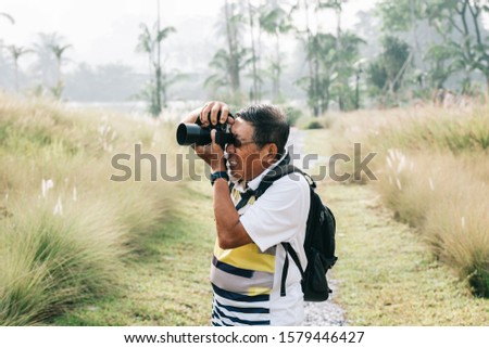 Asian Chinese mature male taking outdoor photographs with digital DSLR camera. Enjoying retired life.