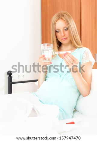 Pregnant woman sitting on bed  with thermometer 