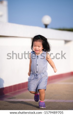 Vertical photos. An Asian girl is playing, leaping forward, joyfully on a clear day. The girl smiled sweetly in a good mood. Baby age 2 years and 9 months old.