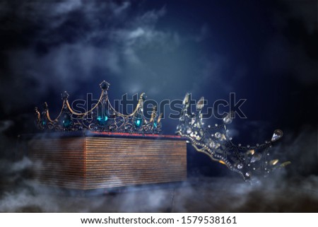 low key image of beautiful queen/king crown over old book and wooden table. vintage filtered. fantasy medieval period. mist and fog