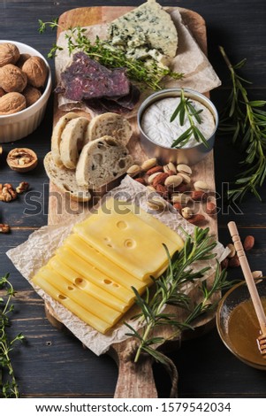 Tasting different types of cheese, honey, nuts, herbs and sausages. Several varieties of cheese on a wooden board. Delicatessen for a romantic dinner.