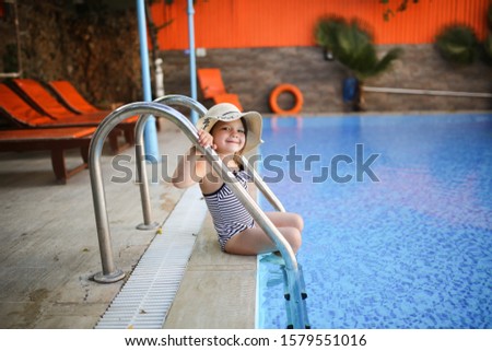 Funny emotional girl child in a striped swimsuit plays by the pool. Concept summer vacation with children and child safety. Child alone near outdoor pool