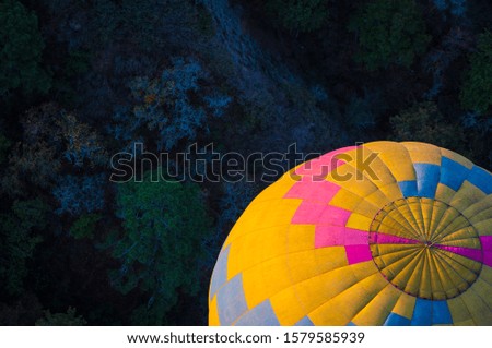 Aerial shot of yellow, blue, pink and gray aersotatic balloon with a background of trees in blue tones that give great contrast on a flight through Hidalgo Mexico