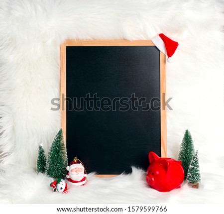Clean blank blackboard with piggy bank, santa and fir trees over white fur background. Christmas Holiday decorative concept with copy space for text. aving money for Xmas holidays. 