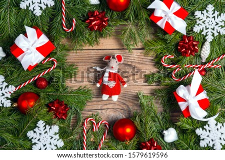Toy mouse as a symbol of the year with fir branches, gifts and decorations on old wooden boards. 