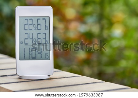 Best personal weather station device with weather conditions inside and outside on foliage background. Home digital weather forecast concept with temperature and humidity.