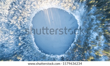 Аerial view of snow covered forest around beautiful lake. Rime ice and hoar frost covering trees. Scenic winter landscape near Helsinki, Finland.