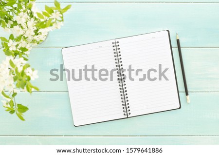 Sprig with white flowers on mint background with notepad and pencil. Spring concept. Overhead shots