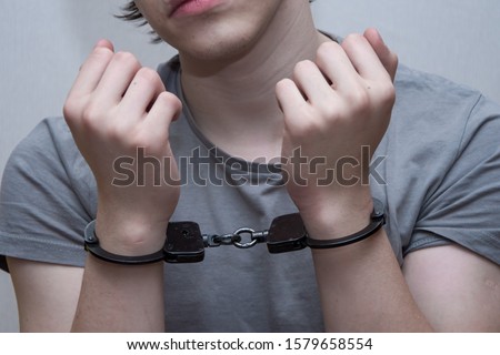 A handcuffed teenager sits on a grey background. Juvenile delinquent, criminal liability of minors. Members of youth criminal groups and gangs.