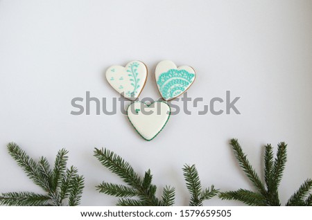 Gingerbread cookies in the shape of a white heart with a pattern lie on a white background in the center. At the bottom of the background are branches of spruce. horizontal image. Flat lay