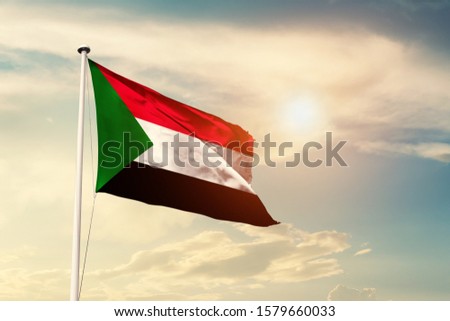 Sudan national flag cloth fabric waving on the sky with beautiful sun light - Image Royalty-Free Stock Photo #1579660033