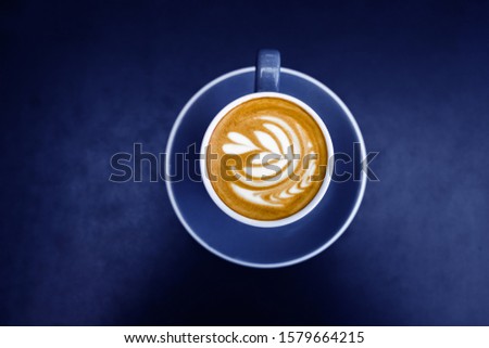 Blue cup of fresh cappuccino with latte art on dark metal table background. Empty place for text, copy space. Coffee addiction concept. Top view from above. Trend glow bright color.