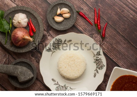Flat lay of Malay design traditional glass plate with white rice. Asian food concept picture.  Malay cuisine. Stone mortar and pestle with onion and garlic.