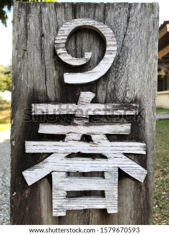 A weathered wooden post with a white wooden number 1 on top in Thai and the word room translation from Japanese Katanana below.