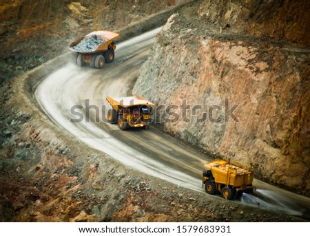 Three trucks in a busy modern gold mine in Kalgoorlie, Western Australia. One water truck and two large haul trucks transport gold ore from an open cast mine. - All logos removed. Royalty-Free Stock Photo #1579683931