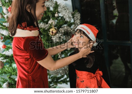 mother helping her daughter to put on santa hat