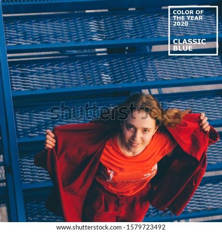 Color of the year 2020 Classic Blue pantone. Young woman in red mantle posing on blue background. Millennial concept.