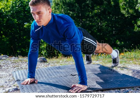 Strong handsome blonde athlete doing push ups on top of and mountain while enjoying the amazing view at the lake down in the valley.