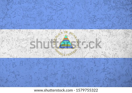 Nicaragua flag depicted in bright paint colors on old relief plastering wall. Textured banner on rough background
