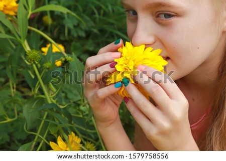 Children's colorful summer manicure on a girl with blonde hair on a background of green vegetation in summer.