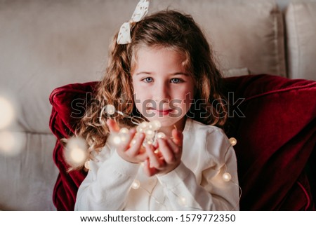 beautiful kid girl at home playing with garland of lights. Christmas concept