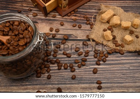 Wooden spoon in a glass jar with coffee beans, coffee grinder, pieces of brown sugar on a wooden background. Close up.