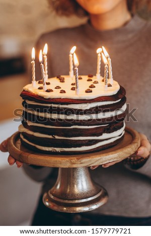 young attractive blond girl with gorgeous model smile holds cake. Emotions of a happy birthday girl from an unexpected gift: homemade cake with burning candles, selective focus, noise effect
