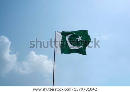 The national flag of Pakistan flying in the blue sky with clouds