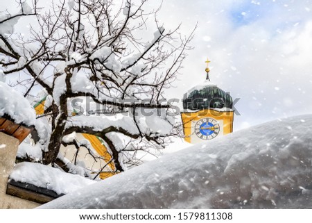 Roof of old building covered with thick snow drift layer after heavy snowfall blizzard and austrian Kufstein town hall .tower with clocks on background on bright sunny winter day winter weather scene