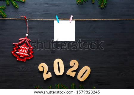 New Year greeting card. Brown cardboard sheet of paper hanging on a rope with a clothespin on a dark wooden background. Christmas toy. 2020.